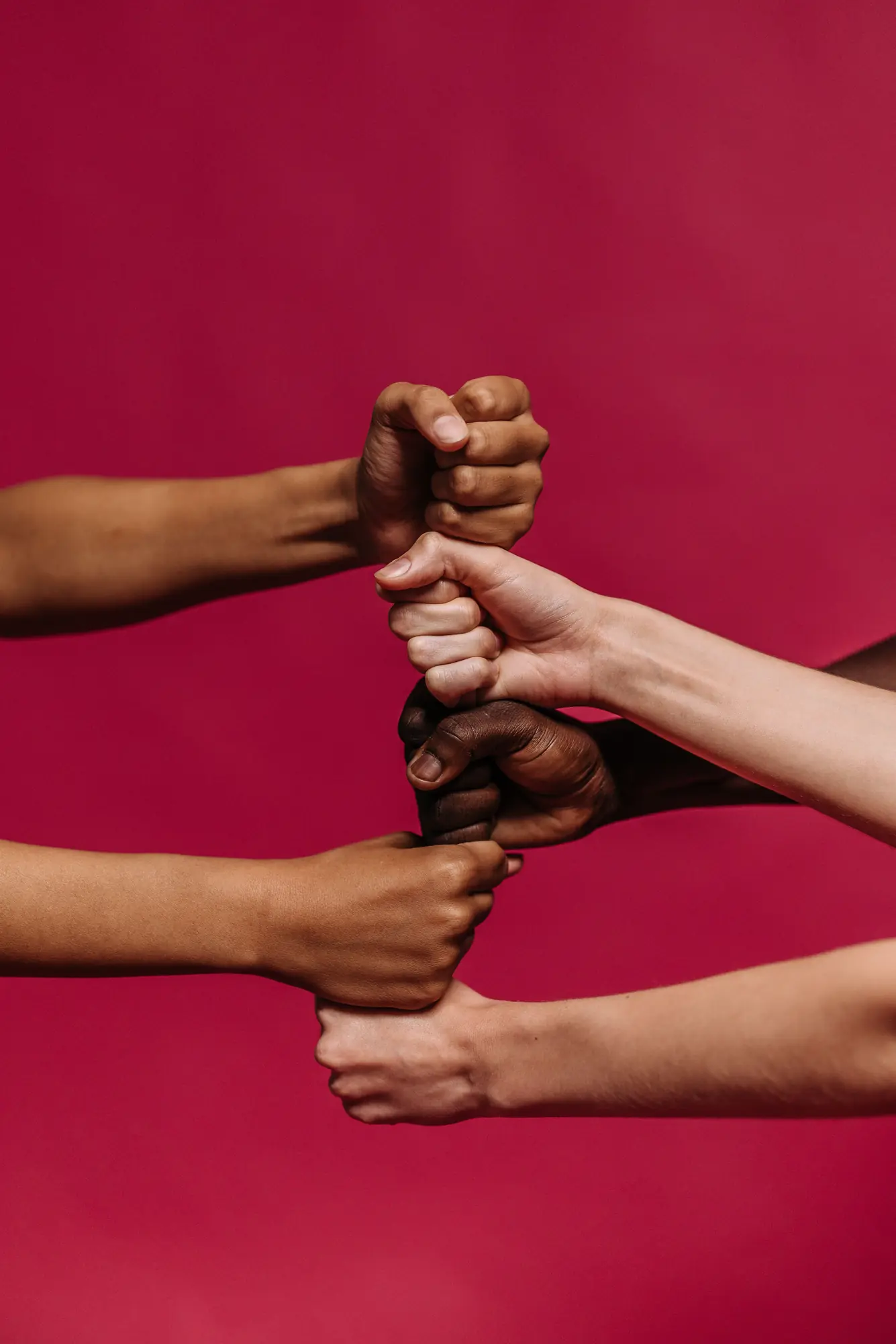 Four arms reaching in from the edges of the frame, each hand gripping the wrist of the next.