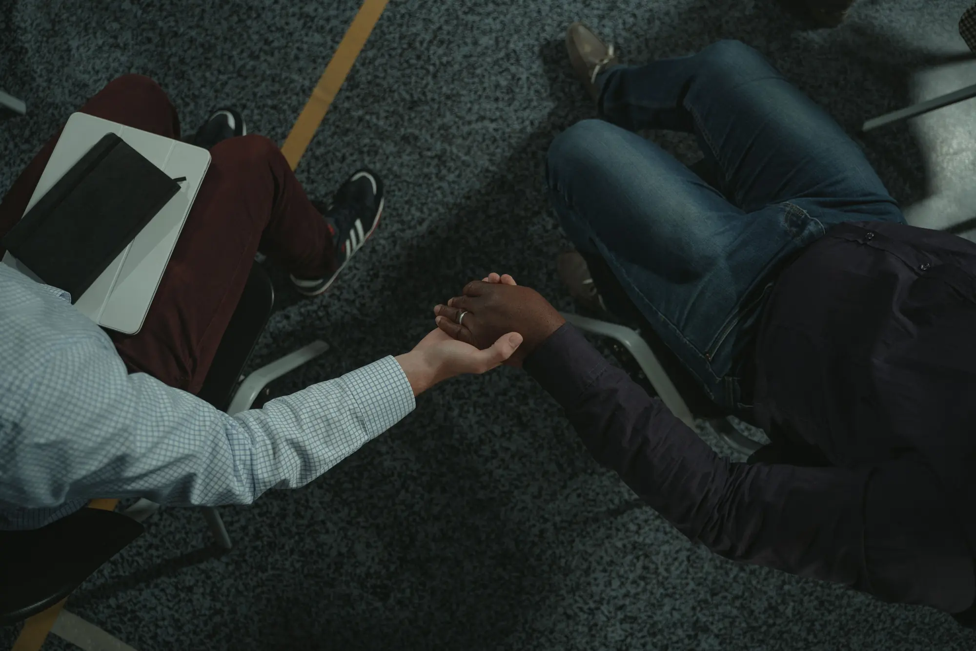 Two seated people photographed from above, one reaching across to hold the other's hand.