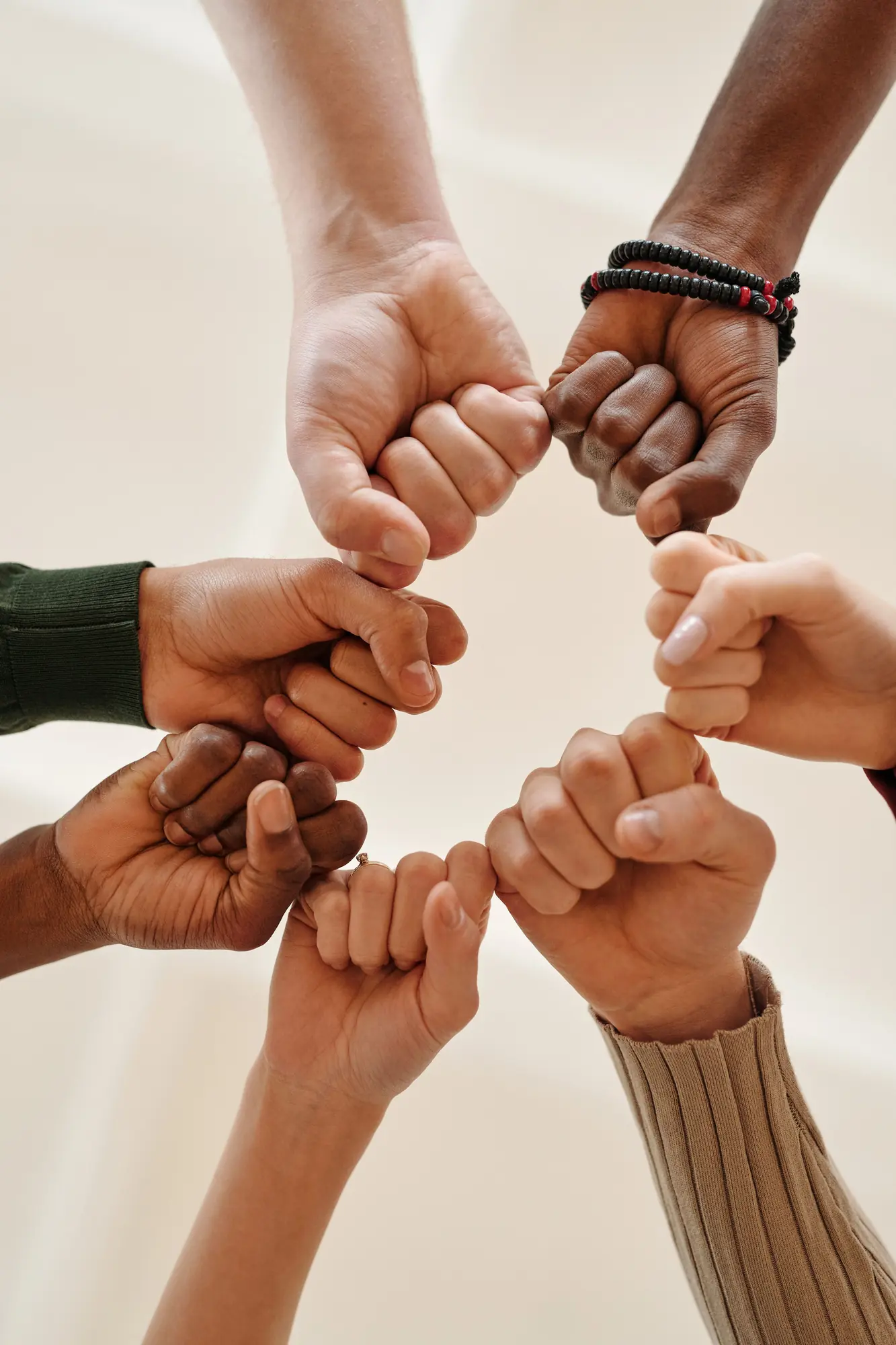 Six hands of different skin tones meeting in a ring, each fist touching the next.