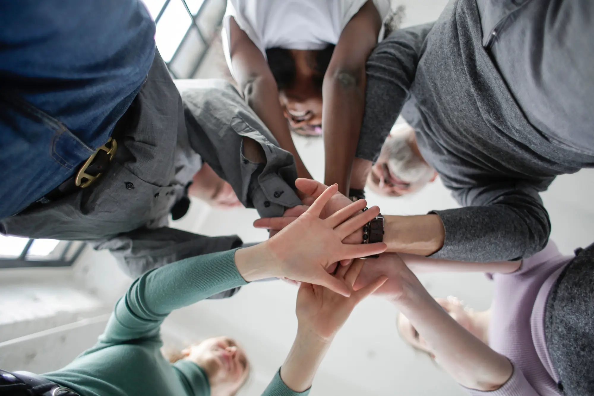 Several people standing in a circle indoors, stacking their hands together in the centre.