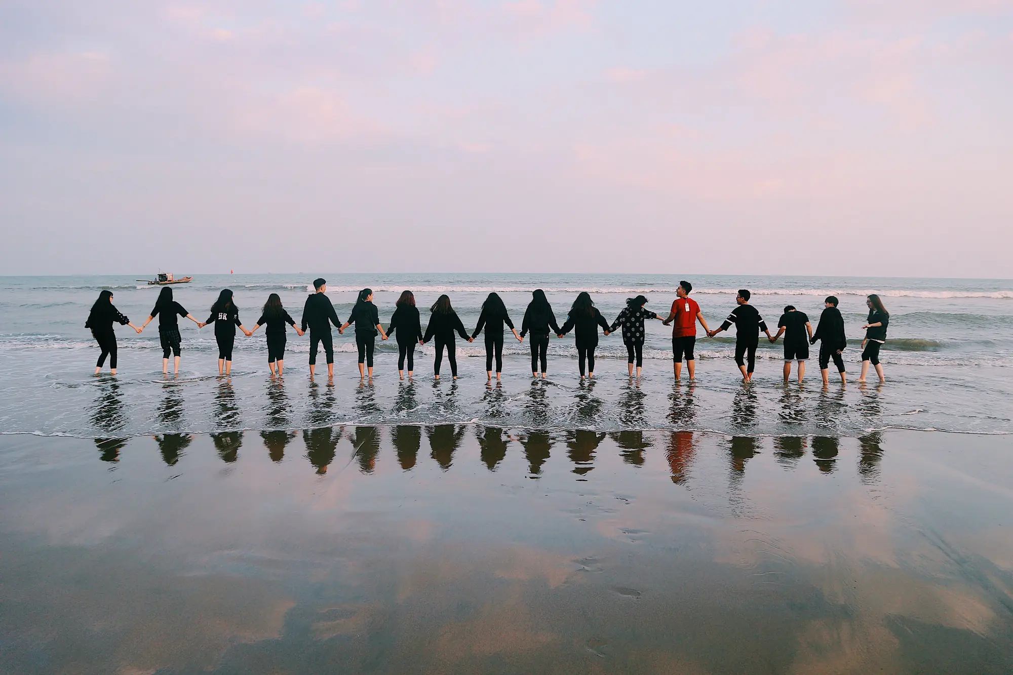 A long line of people standing in shallow water at dusk, holding hands, facing the sea.